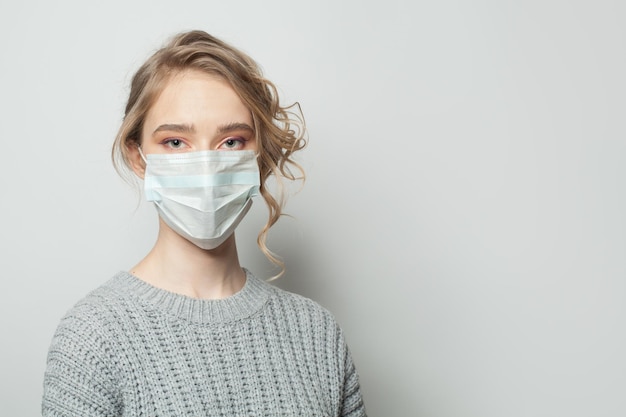Mujer bonita con una máscara facial sobre un fondo blanco Mujer con una mascarilla médica Concepto de protección contra la epidemia de gripe y el virus