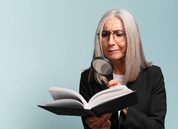 Mujer bonita mayor con un libro y una lupa. concepto de búsqueda