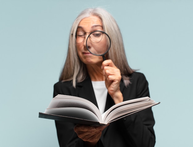 Mujer bonita mayor con un libro y una lupa.