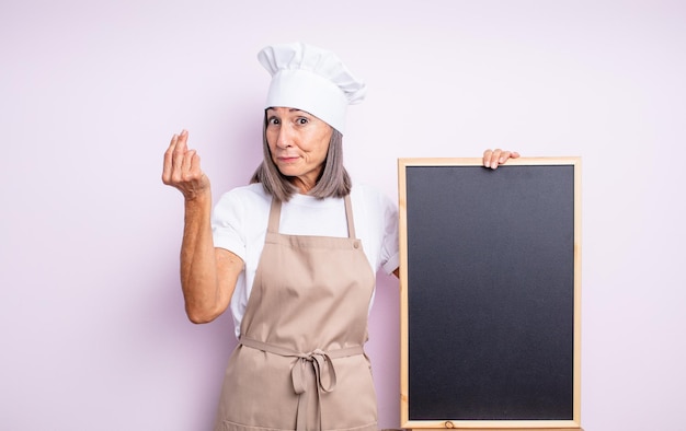 Mujer bonita mayor que hace el gesto del capice o del dinero, diciéndole que pague. concepto de chef y pizarra