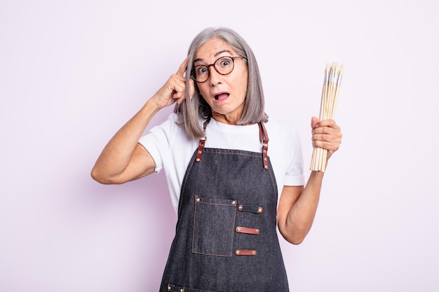 Mujer bonita mayor que parece sorprendida, dándose cuenta de un nuevo pensamiento, idea o concepto. artista con pinceles