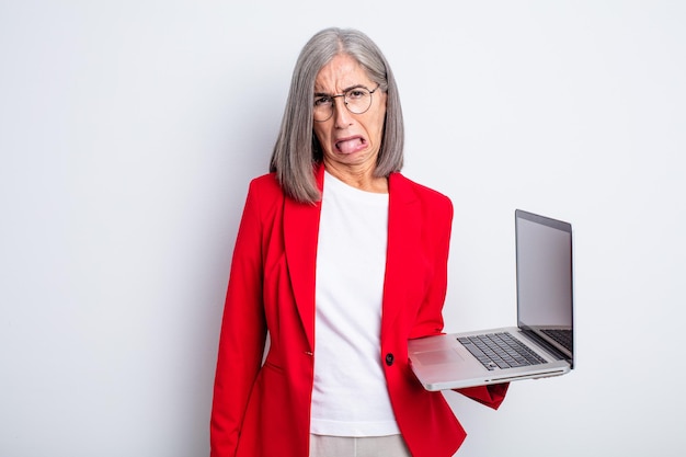 Mujer bonita mayor que se siente disgustada e irritada y saca la lengua. concepto de negocio y portátil