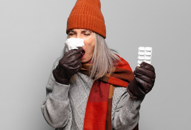 Mujer bonita mayor con una tableta de píldoras con ropa de invierno. concepto de gripe