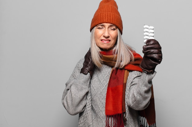 Mujer bonita mayor con una tableta de píldoras con ropa de invierno. concepto de gripe