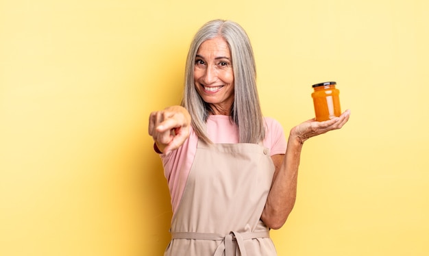 Mujer bonita de mediana edad apuntando a la cámara eligiéndote. Mermelada de durazno