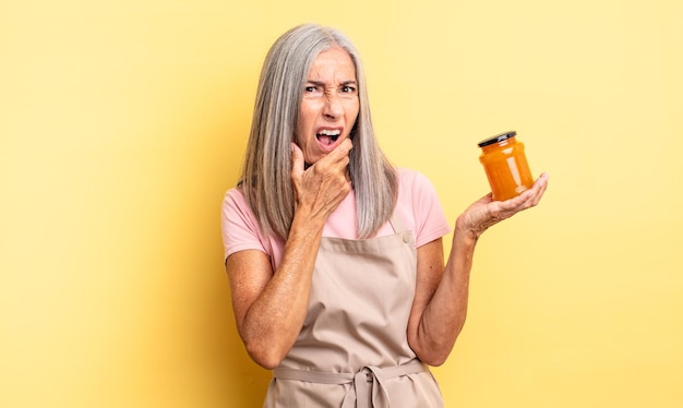 Mujer bonita de mediana edad con la boca y los ojos bien abiertos y la mano en la barbilla. Mermelada de durazno