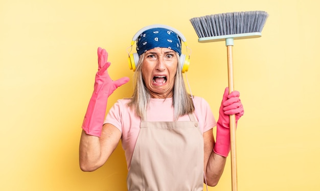 Mujer bonita de mediana edad gritando con las manos en el aire. concepto de hogar y escoba