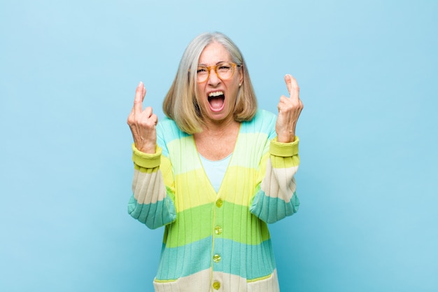 Mujer bonita de mediana edad o mayor cruzando los dedos ansiosamente y esperando buena suerte con una mirada preocupada