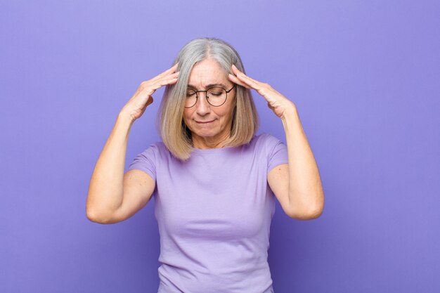 Mujer bonita de mediana edad o mayor que parece concentrada, reflexiva e inspirada, lluvia de ideas e imaginación con las manos en la frente