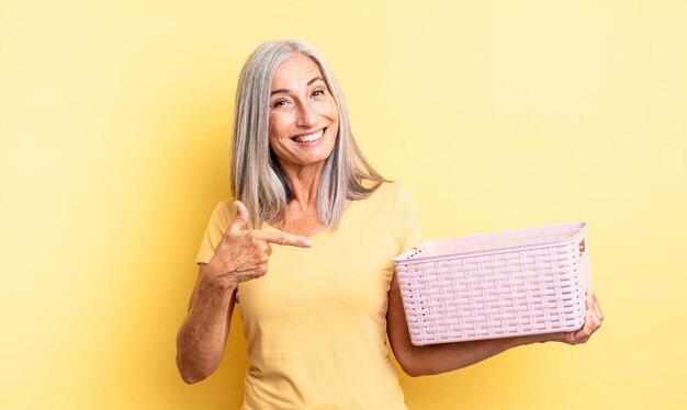 Mujer bonita de mediana edad que parece emocionada y sorprendida apuntando hacia un lado. concepto de cesta vacía