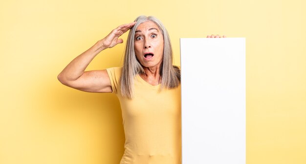 Mujer bonita de mediana edad que parece feliz, asombrada y sorprendida. concepto de lienzo vacío