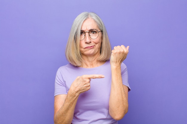 Mujer bonita de mediana edad que parece impaciente y enojada, señalando el reloj