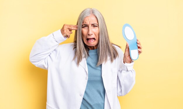 Mujer bonita de mediana edad que parece infeliz y estresada, gesto de suicidio haciendo signo de pistola. concepto de podólogo