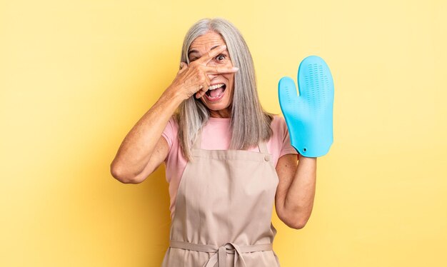 Mujer bonita de mediana edad que parece sorprendida, asustada o aterrorizada, cubriendo la cara con la mano. concepto de manopla de horno