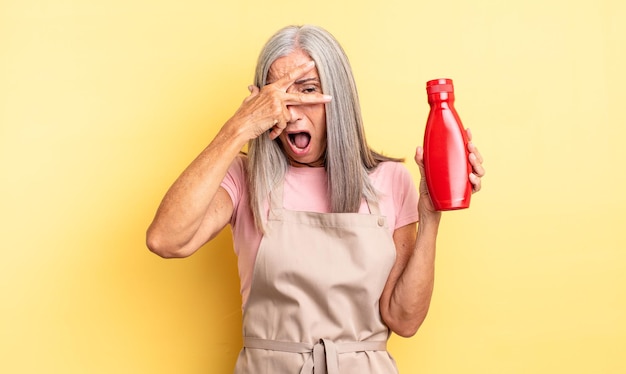 Mujer bonita de mediana edad que parece sorprendida, asustada o aterrorizada, cubriendo la cara con la mano. concepto de salsa de tomate