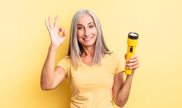 Mujer bonita de mediana edad que se siente feliz, mostrando aprobación con gesto bien. concepto de linterna