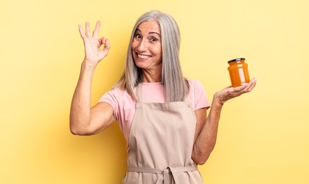 Mujer bonita de mediana edad que se siente feliz, mostrando aprobación con gesto bien. Mermelada de durazno