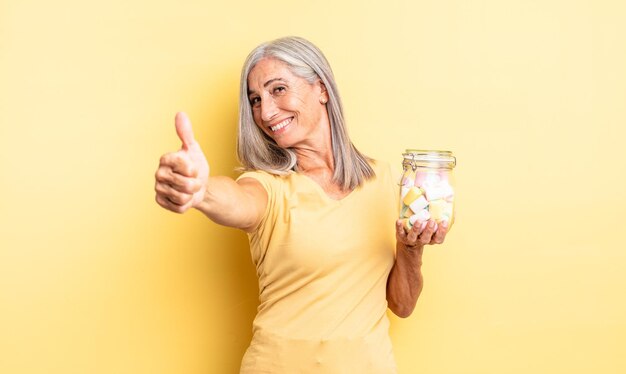 Mujer bonita de mediana edad que se siente orgullosa, sonriendo positivamente con los pulgares hacia arriba. concepto de botella de caramelos