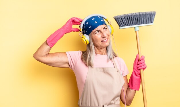 mujer bonita de mediana edad que se siente perpleja y confundida, rascándose la cabeza. concepto de hogar y escoba