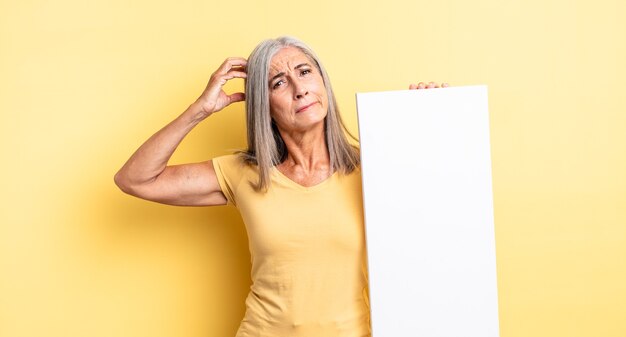 Mujer bonita de mediana edad que se siente perpleja y confundida, rascándose la cabeza. concepto de lienzo vacío