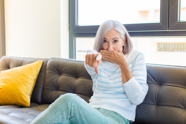 Mujer bonita de mediana edad riéndose de ti, señalando al frente y burlándose o burlándose de ti