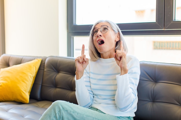 Mujer bonita de mediana edad sintiéndose asombrado y con la boca abierta apuntando hacia arriba