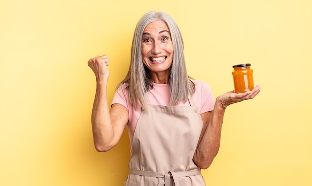 Mujer bonita de mediana edad sintiéndose conmocionada, riendo y celebrando el éxito. Mermelada de durazno