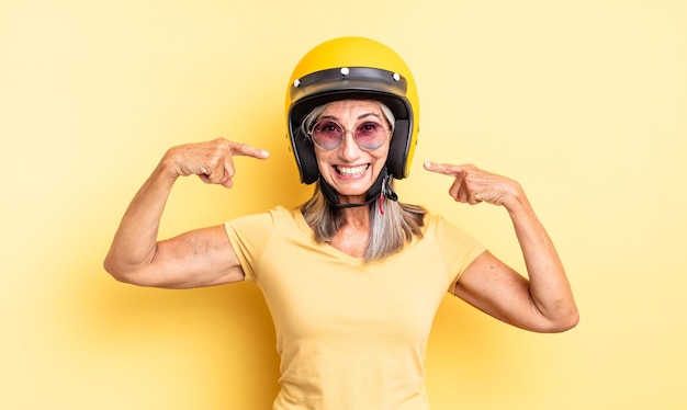 Mujer bonita de mediana edad sonriendo con confianza apuntando a su propia sonrisa amplia. concepto de casco de moto