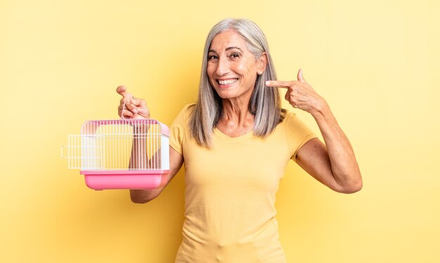 Mujer bonita de mediana edad sonriendo con confianza apuntando a su propia sonrisa amplia. concepto de jaula o cárcel para mascotas