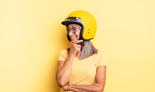 Mujer bonita de mediana edad sonriendo con una expresión de confianza feliz con la mano en el concepto de casco de moto barbilla