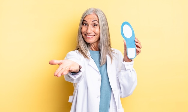 Mujer bonita de mediana edad sonriendo felizmente con amabilidad y ofreciendo y mostrando un concepto de podólogo