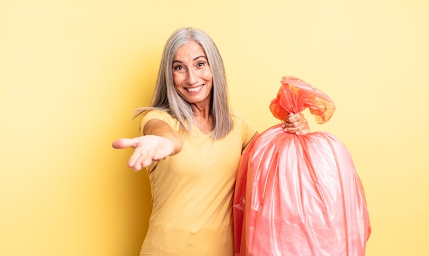 Mujer bonita de mediana edad sonriendo felizmente con amable y ofreciendo y mostrando un concepto. bolsa de plástico para garbaje