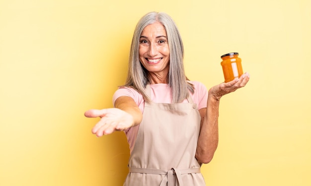 Mujer bonita de mediana edad sonriendo felizmente con amable y ofreciendo y mostrando un concepto. Mermelada de durazno