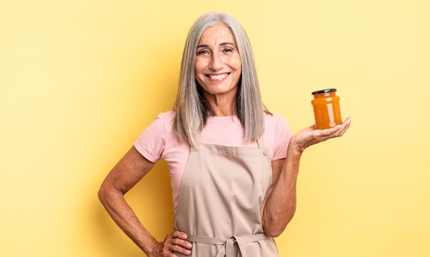 Mujer bonita de mediana edad sonriendo felizmente con una mano en la cadera y confiada. Mermelada de durazno