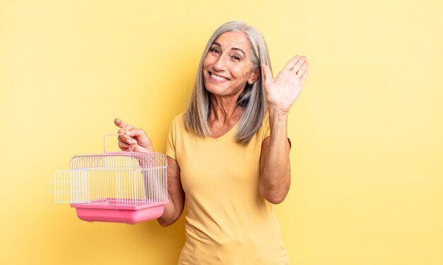 Mujer bonita de mediana edad sonriendo felizmente, saludando con la mano, dándote la bienvenida y saludándote. concepto de jaula o cárcel para mascotas