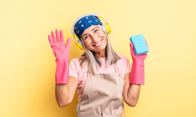 Mujer bonita de mediana edad sonriendo felizmente, saludando con la mano, dándote la bienvenida y saludándote. limpiador estropajo