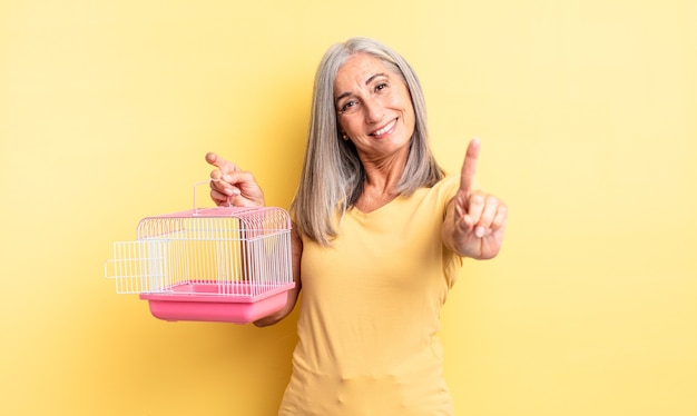 mujer bonita de mediana edad sonriendo y mirando amigable, mostrando el número uno. concepto de jaula o cárcel para mascotas