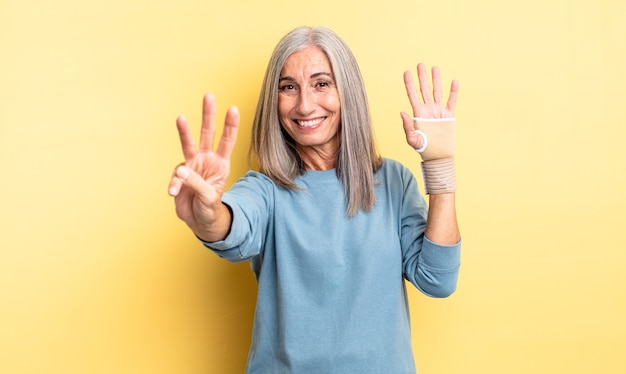 Mujer bonita de mediana edad sonriendo y mirando amigable, mostrando el número tres. concepto de vendaje de mano