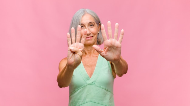 Mujer bonita de mediana edad sonriendo y mirando amigablemente, mostrando el número ocho u octavo con la mano hacia adelante, contando hacia atrás