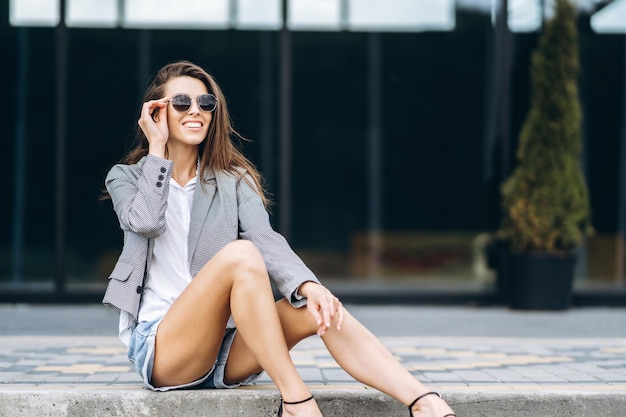 Mujer bonita de moda sentada en la calle de la ciudad