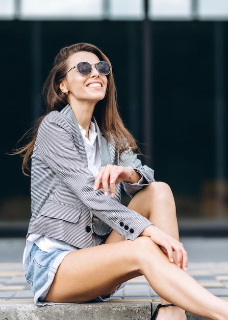 Mujer bonita de moda sentada en la calle de la ciudad