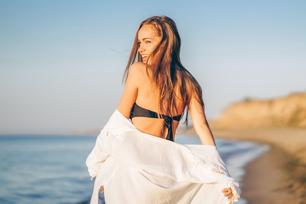 Mujer bonita morena con una camisa blanca posando en la playa