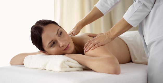 Mujer bonita morena disfrutando del procedimiento de masaje de espalda en el salón de spa. Concepto de belleza.