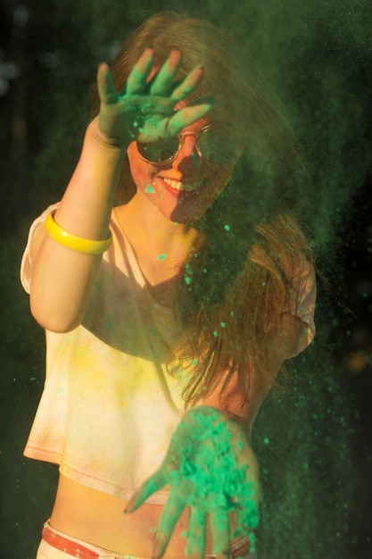 Mujer bonita morena con gafas de sol divirtiéndose con polvo verde de Holi en el parque