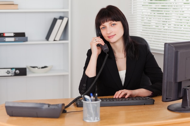 Mujer bonita morena en el teléfono mientras trabajaba en una computadora