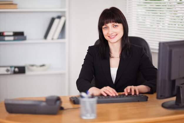 Mujer bonita morena trabajando en una computadora mientras está sentado en un escritorio