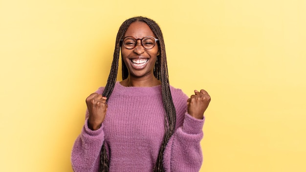 Mujer bonita negra afro gritando triunfalmente, riendo y sintiéndose feliz y emocionada mientras celebra el éxito