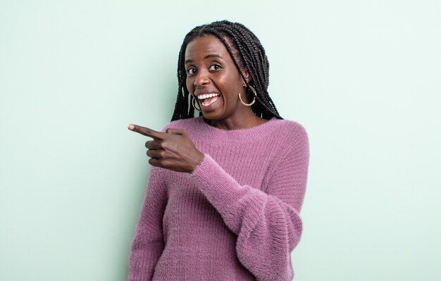 Mujer bonita negra que parece emocionada y sorprendida apuntando hacia un lado y hacia arriba para copiar el espacio