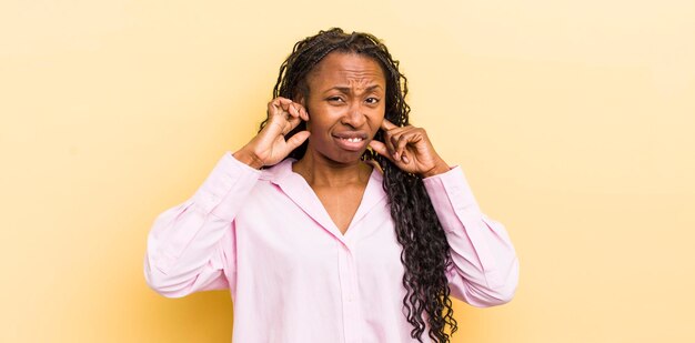 Mujer bonita negra que parece enojada, estresada y molesta cubriendo ambos oídos con un ruido ensordecedor o música a todo volumen