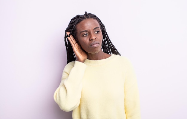 Mujer bonita negra que parece seria y curiosa, escuchando, tratando de escuchar una conversación secreta o chismes, escuchando a escondidas